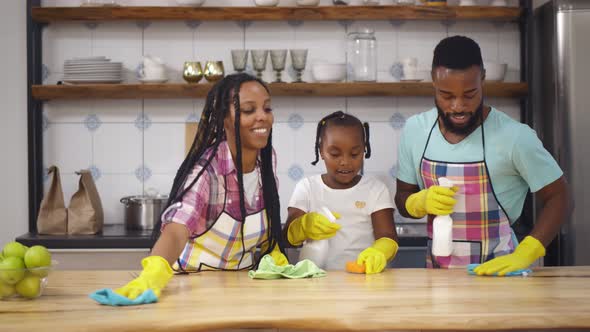 Happy African Family in Apron and Rubber Gloves Cleaning Kitchen Surface Together