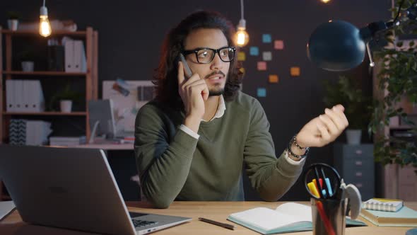 Joyful Businessman Speaking on Mobile Phone in Workplace at Night Smiling Discussing Business