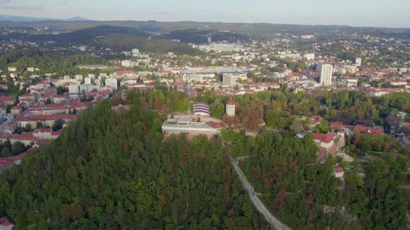 Aerial view above landmark Glokenturm tower on Graz's Schloßberg hilltop woodland park panning acros