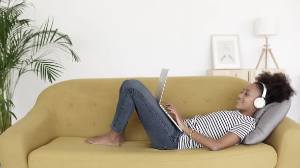 Relaxed Young African Woman Working on Laptop Computer While Lying on Sofa