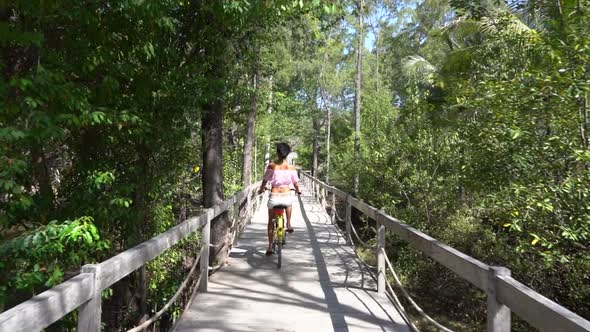 Following Shot of Cute Girl Riding a Bicycle on the Rural Wooden Bridge in Beautiful Tropic Nature