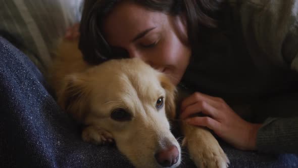 Caucasian woman kissing and cuddling her pet dog sitting on sofa at home