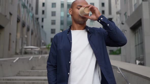 Confident Ethnic Pedestrian Drinking Hot Beverage and Using Smartphone