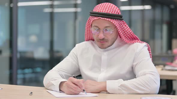 Pensive Middle Aged Arab Man Writing on Paper