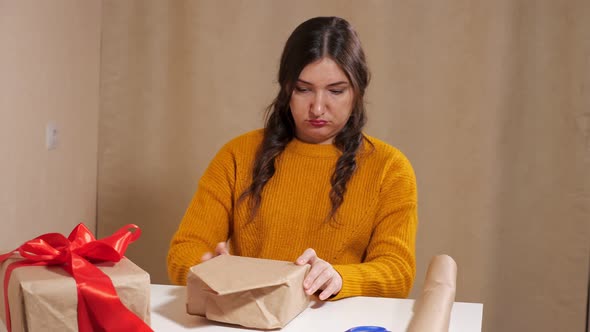 Upset Young Woman Trying to Wrap Gift in Kraft Paper