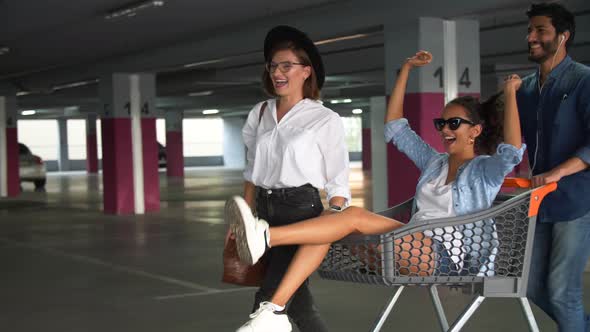 Young People Having Fun, Racing On Shopping Trolley At Parking