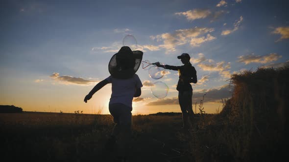 Young Mom and Little Son in the Sunset Catches Soap Bubbles in Meadow. Relax with Child in Nature