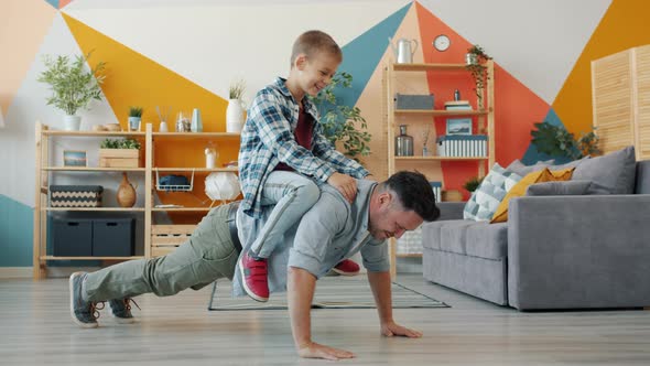 Strong Man Father Doing Push-ups While Son Sitting on His Back Smiling at Home