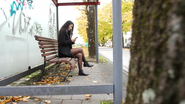 Lonely young woman sitting on the bench at the bus stop.