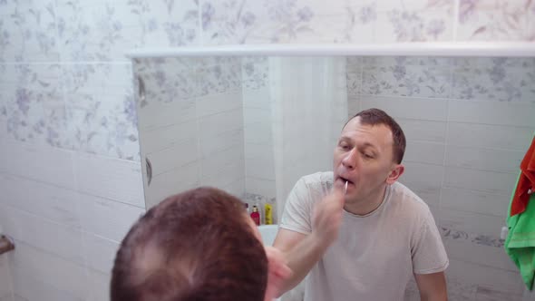 A man plucks hair from his nose, stands in the bathroom in front of a mirror