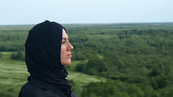 Beautiful Young Muslim Woman in Black Headscarf Walking on Mountain Peak Over Green Forest Valley