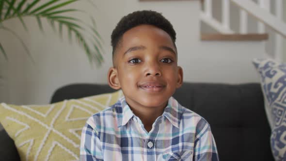 African american boy siting on sofa, looking at camera and smiling