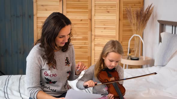 Woman Teaching Little Girl To Play Violin Indoors