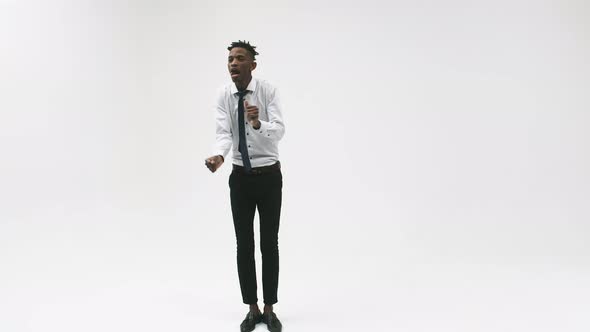 Black man in an office suit dances on the spot in the studio, white background.