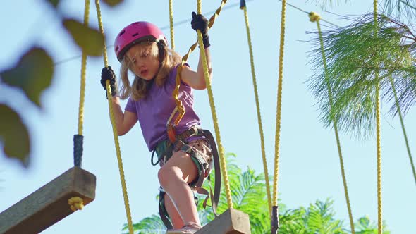 Brave Girl in Helmet Tshirt and Shorts Climbs in Rope Park