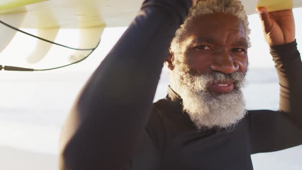 Portrait of happy senior african american man carrying surfboard on sunny beach