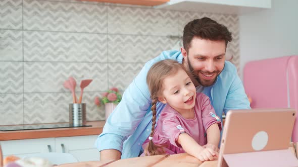 Smiling father and daughter looking cartoon on laptop in the kitchen