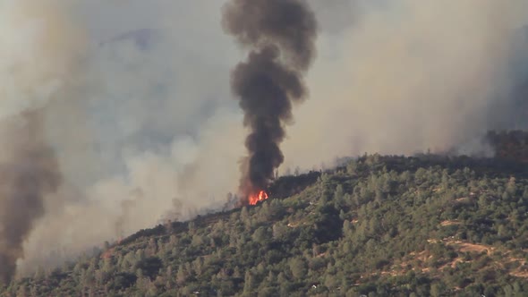 Footage of California wildfire burning on mountains from a distance, flames and smoke rising