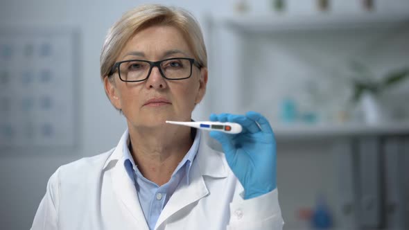 Professional Mature Female Doctor Showing Electronic Thermometer on Camera