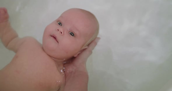 Portrait of Newborn Swimming on a Back in the Bath with Mother Help