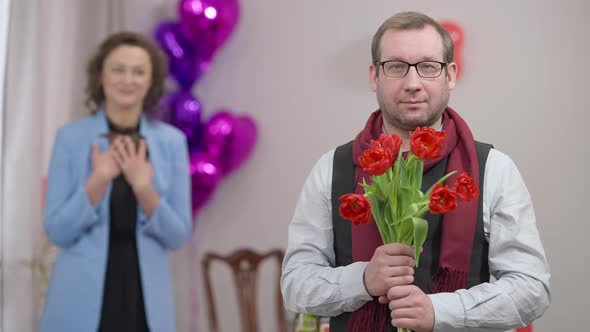 Portrait of Adult Caucasian Stylish Man in Eyeglasses Posing with Bouquet of Flowers Indoors with
