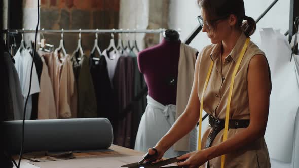 Female Dressmaker Cutting Fabric with Scissors in Sewing Studio