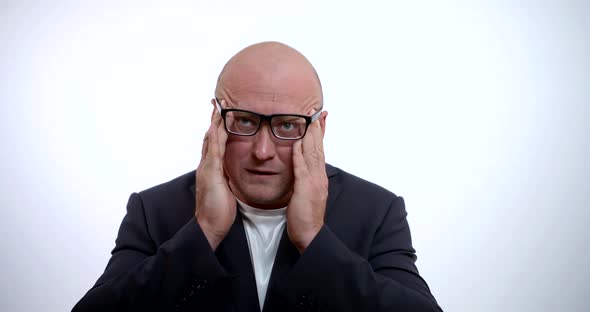 A Portrait of a Sad Bald Man with Glasses, Wearing a Jacket and a Shirt, He Is in the Studio on a