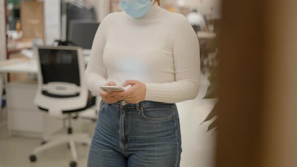 Businesswoman in Medical Face Mask Using the Phone Texting with Both Hands in Office Environment