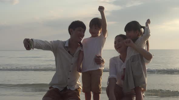 Happy asian family taking a picture with phone on the beach in vacation together.