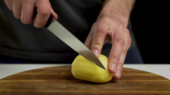 Chef cutting and slicing peeled potato on chopping board, closeup