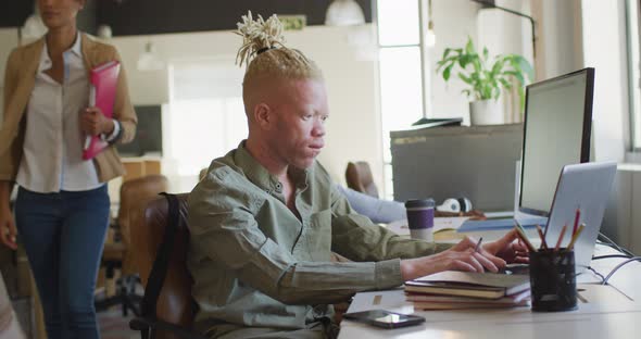Albino african american businessman using laptop in creative office