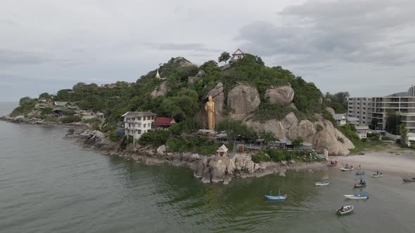 Drone Flying towards Golden Buddha Statue on the rocks at sea