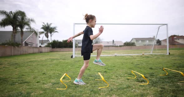 A young athletic girl practices her running form over a set of speed hurdles.