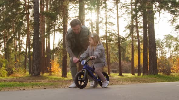 Father Helping Daughter Riding Balance Bicycle