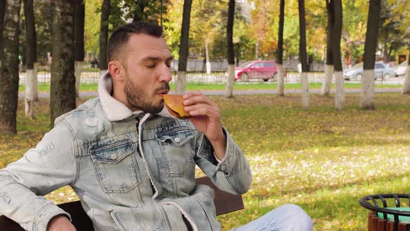 Modern Young Man Sitting on a Bench Eating a Delicious Hamburger