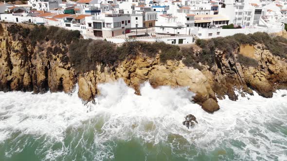 Aerial 4k footage pulling back to reveal ocean waves crashing against the rocky cliffs of Albufeira