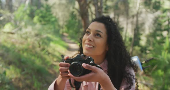 Smiling biracial woman taking photo in forest during hiking in countryside