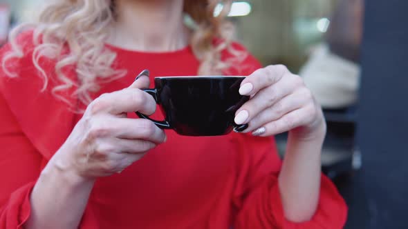 Black Cup of Coffee in Female Hands on a Red Background