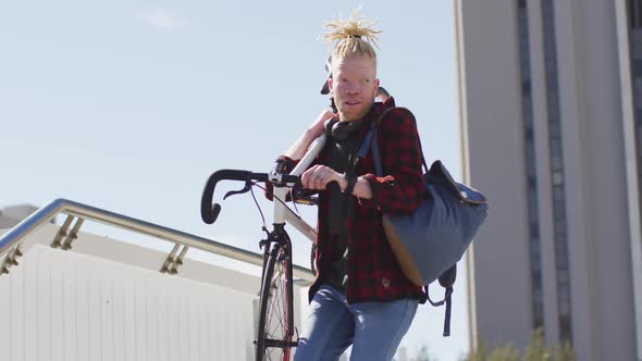 Thoughtful albino african american man with dreadlocks going down stairs with bike