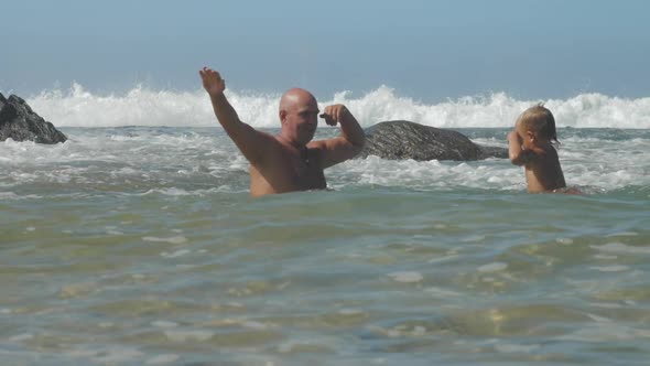 Father and Little Kid Show Muscles Playing in Warm Ocean