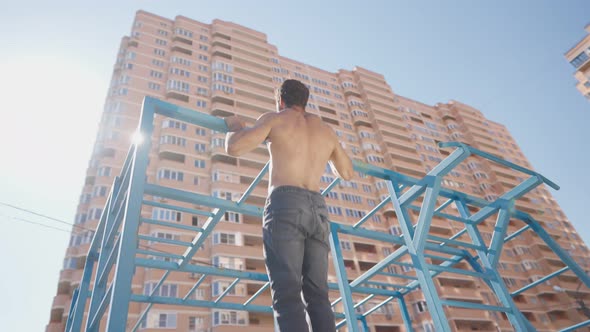 Athletic Man with Naked Torso Pulls Up on Horizontal Bar on Bright Sunny Day