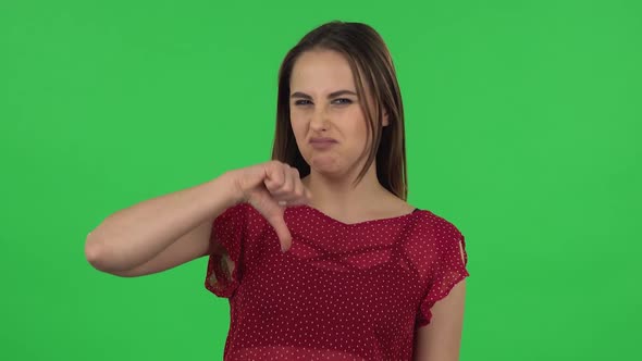Portrait of Tender Girl in Red Dress Is Showing Thumbs Down Gesture. Green Screen
