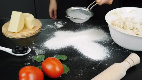 Woman is pouring white flour on black surface in professional modern kitchen