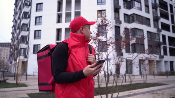 Delivery Guy Wearing Red Uniform While Walking Along Modern Buildings Down City Street with Thermal