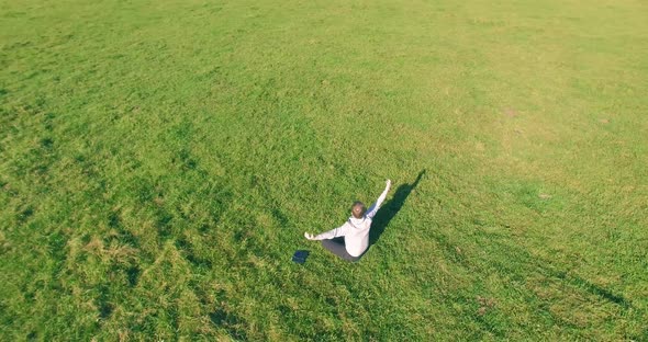 Low Orbital Flight Around Man on Green Grass with Notebook Pad at Yellow Rural Field.