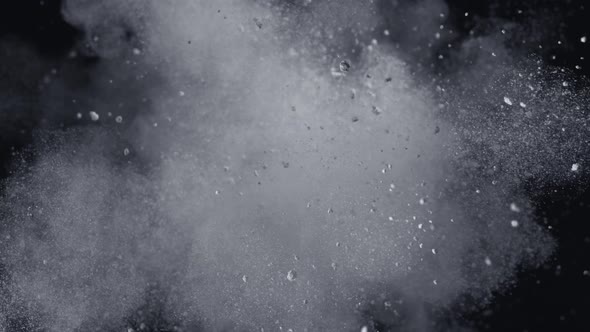 White powder/particles fly after being exploded against black background.  4K 30fps. Slow Motion.