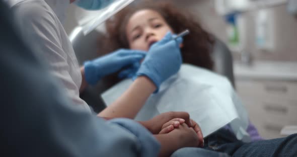 Close Up of African Woman Holding Little Daughter Hand Sitting in Dentist Chair During Teeth Checkup