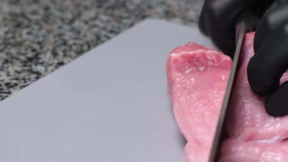 A Chef Cutting a Fresh Pork Tenderloin with a Knife on a Board