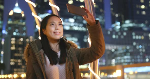 Woman taking photo on smart at night with city background