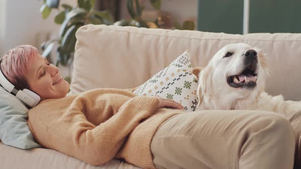 Woman in Headphones Lying on Sofa and Petting Dog